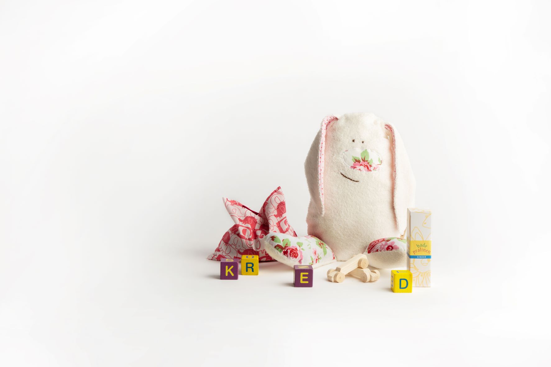 Kuscheltier-Hase mit Stoffkissen und Spielblöcken auf weißem Hintergrund.